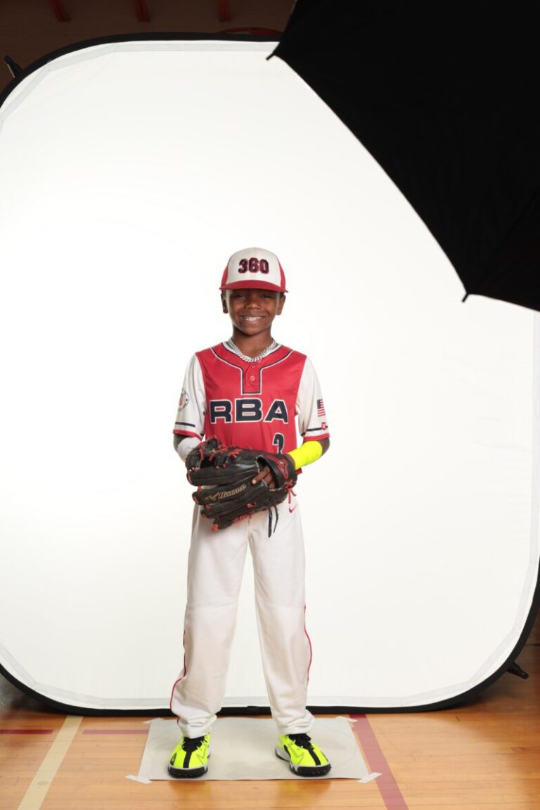 A young boy in a baseball uniform stands in front of a HiLite setup