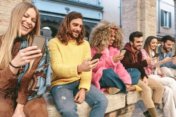 People sit on a ledge outside looking and smiling at their phones
