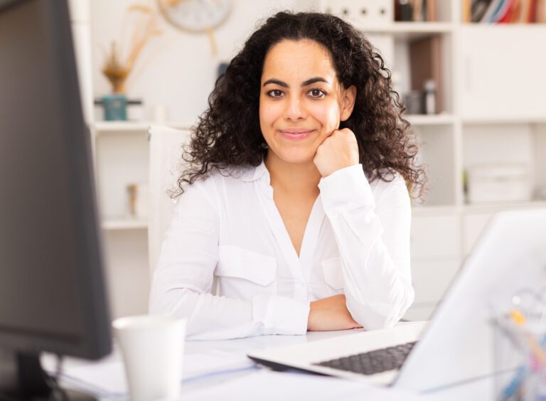 A woman sits smiling in front of a computer