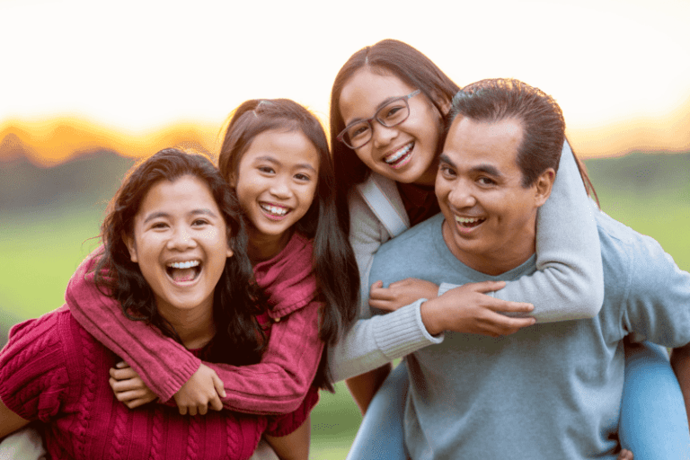 A smiling family with children on their parents' backs outside