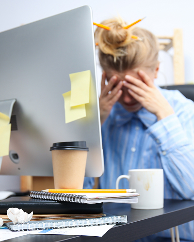 A woman sits at her desk with her head in her hands, stressed out