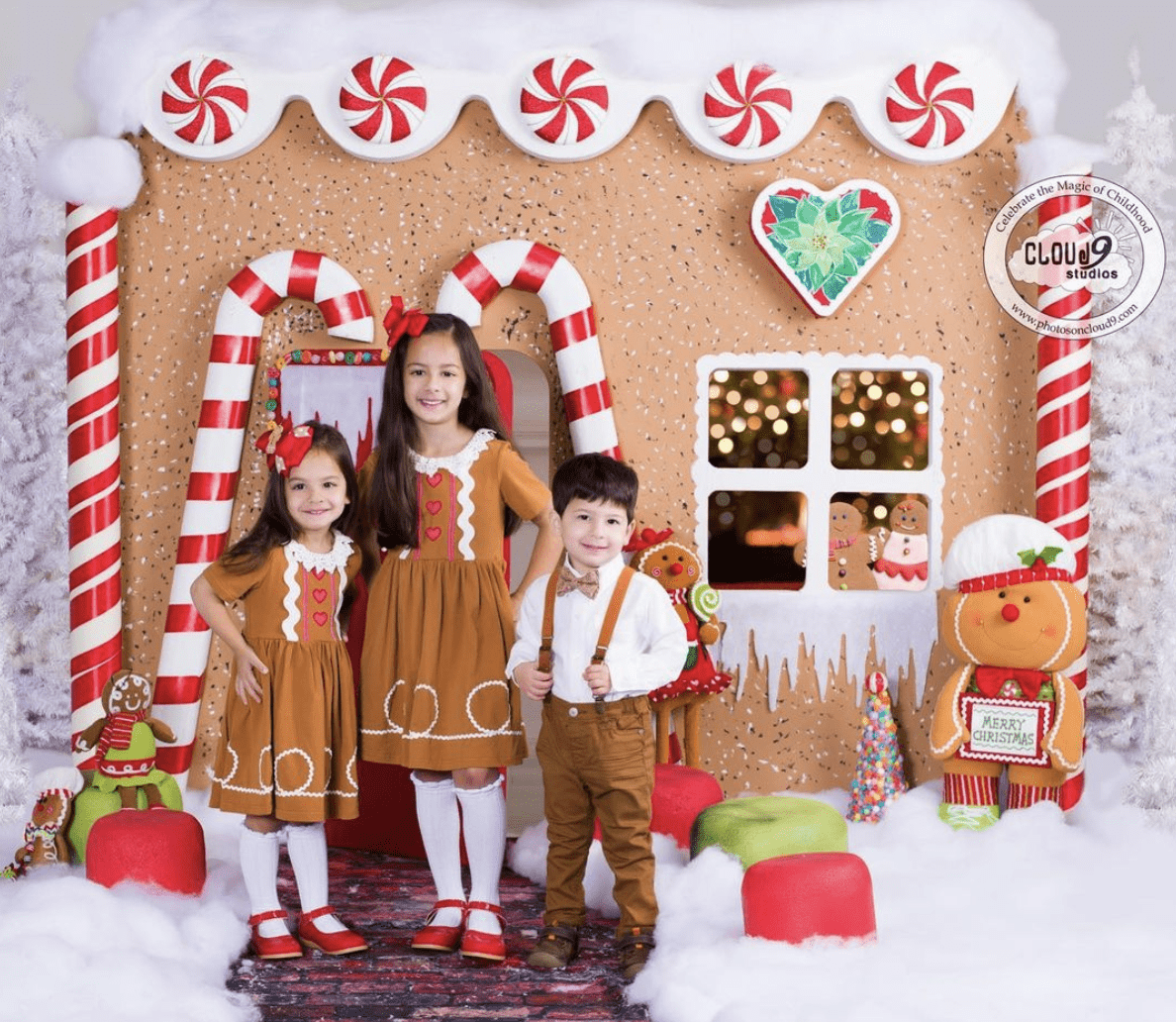 Children pose standing in front of a gingerbread house during the holidays