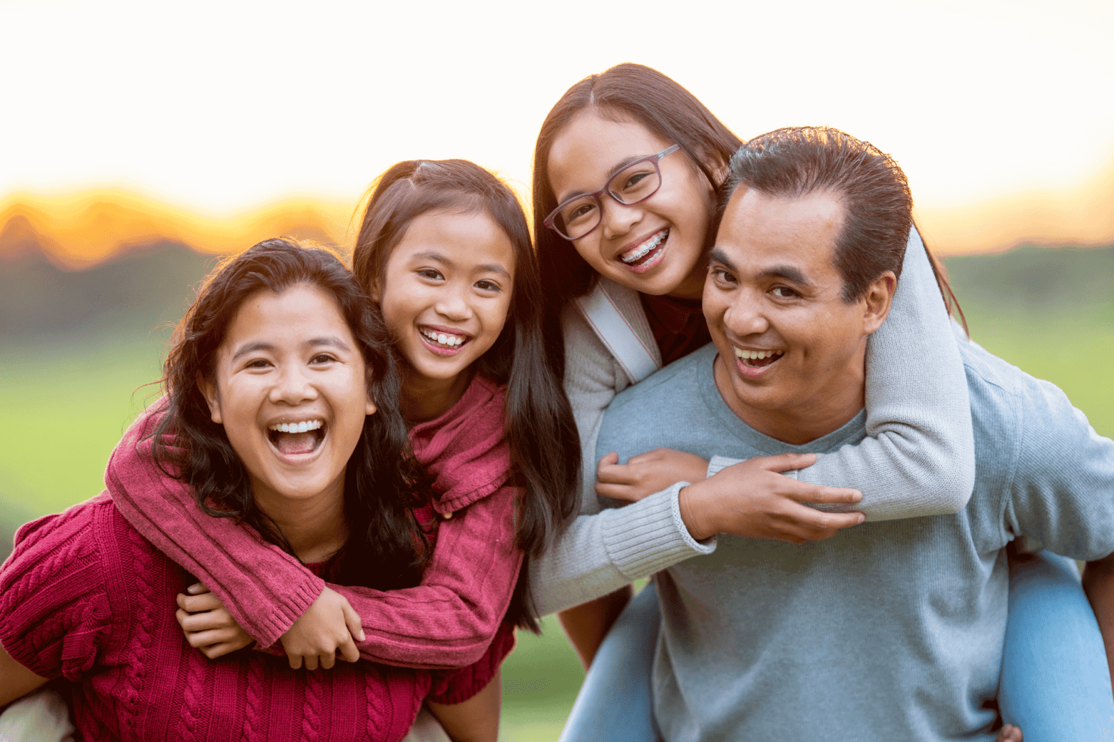 A smiling family with children on their parents' backs outside